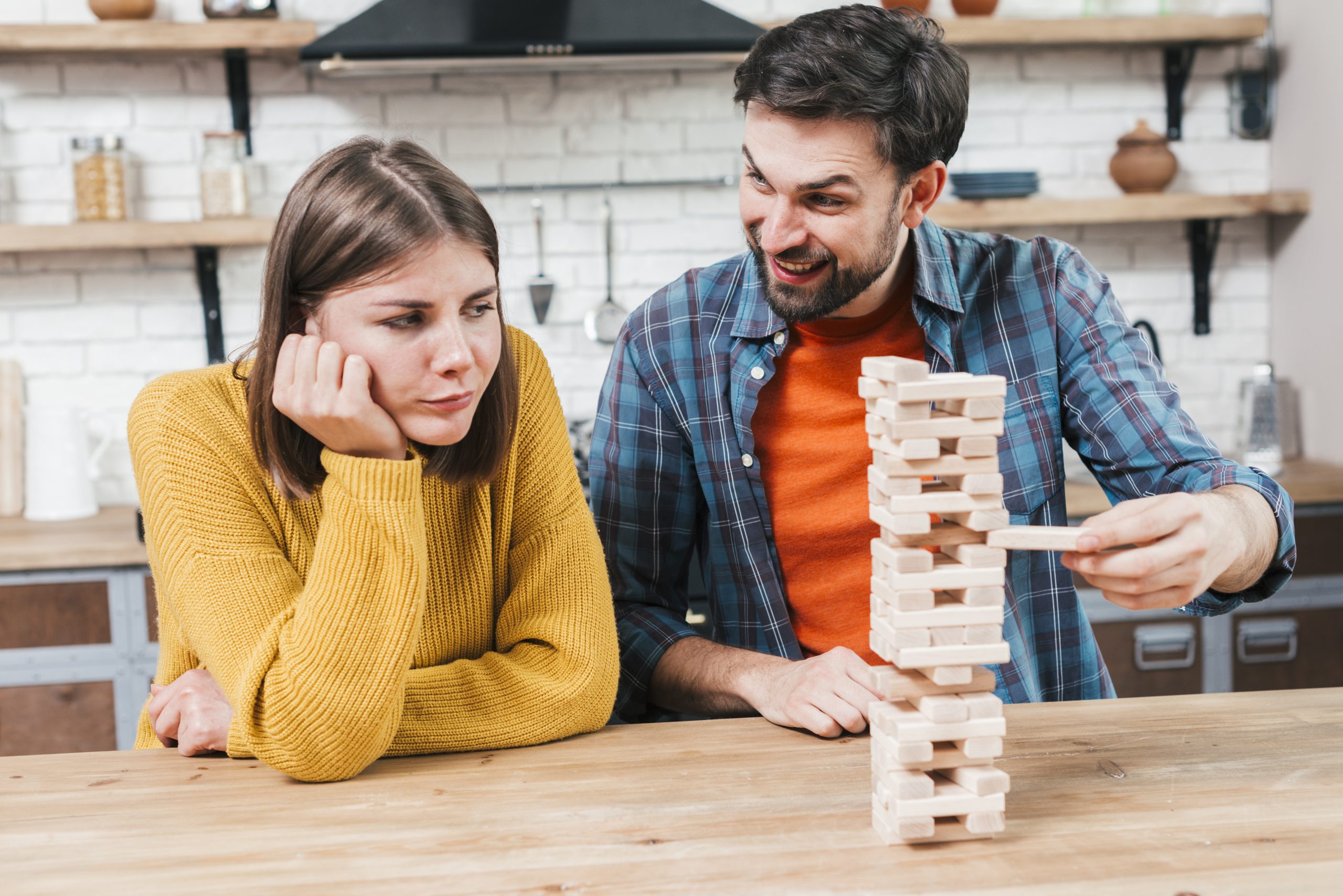 upset-young-woman-looking-happy-man-playing-wooden-stack-desk